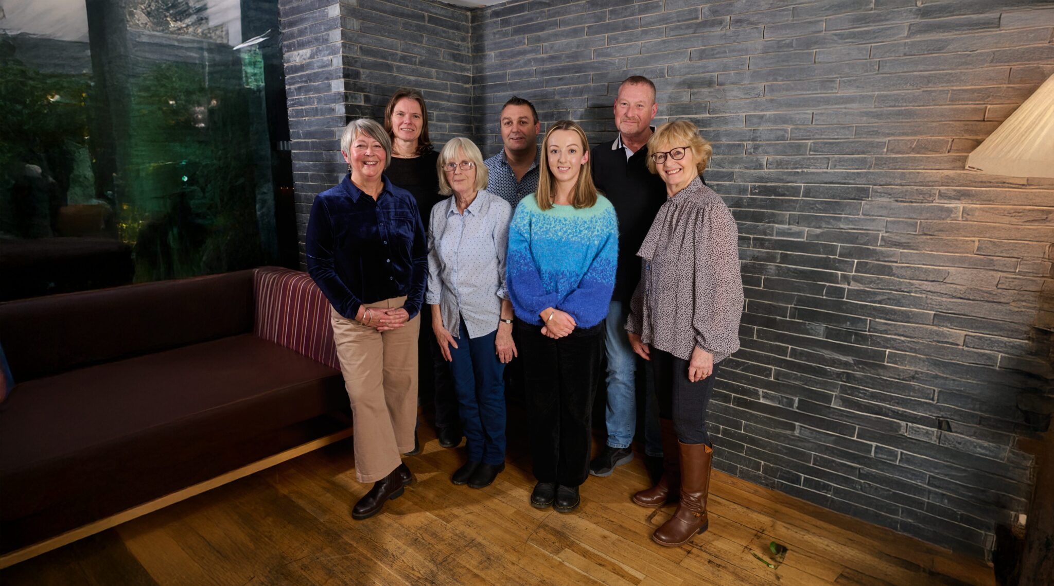 Group of Cardigan Castle staff members smiling in a modern room with stone wall background