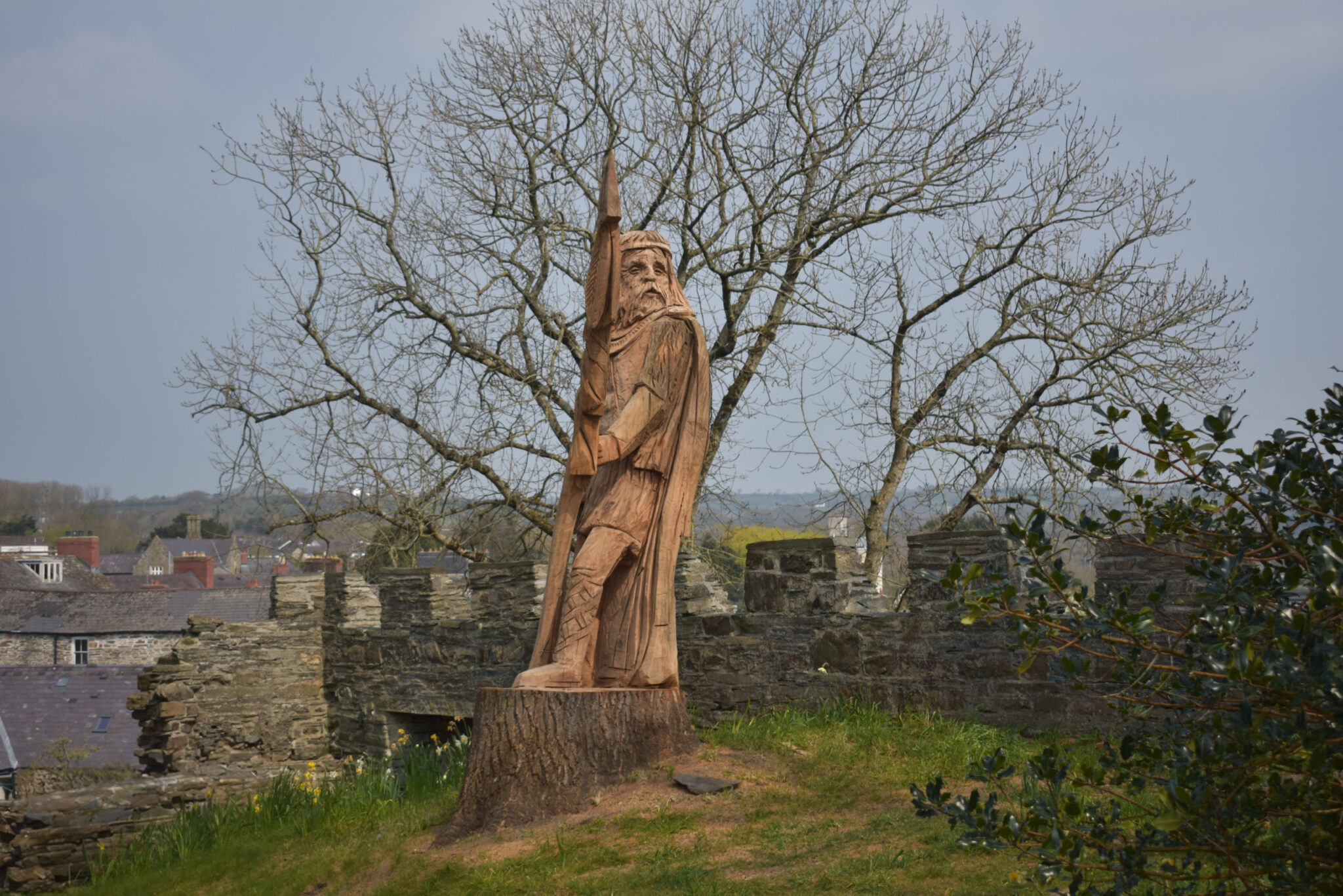 Wooden sculpture of historical figure at Cardigan Castle with rural Welsh landscape in background