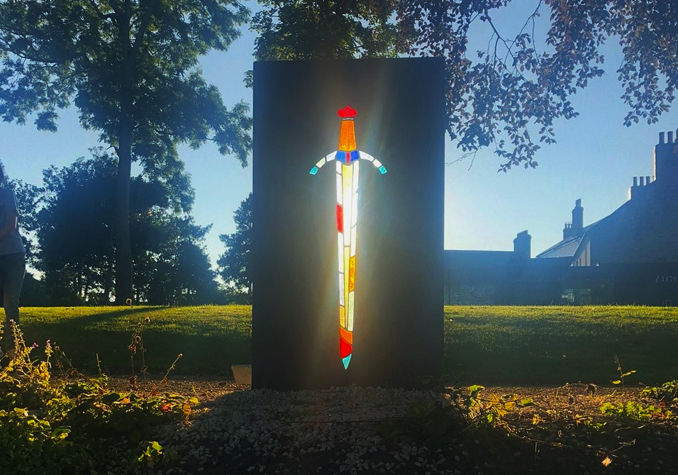 Stained glass art installation at Cardigan Castle grounds during sunset
