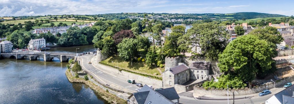 Aerial view of Cardigan Castle by the river Teifi, showcasing historical architecture and lush surroundings.