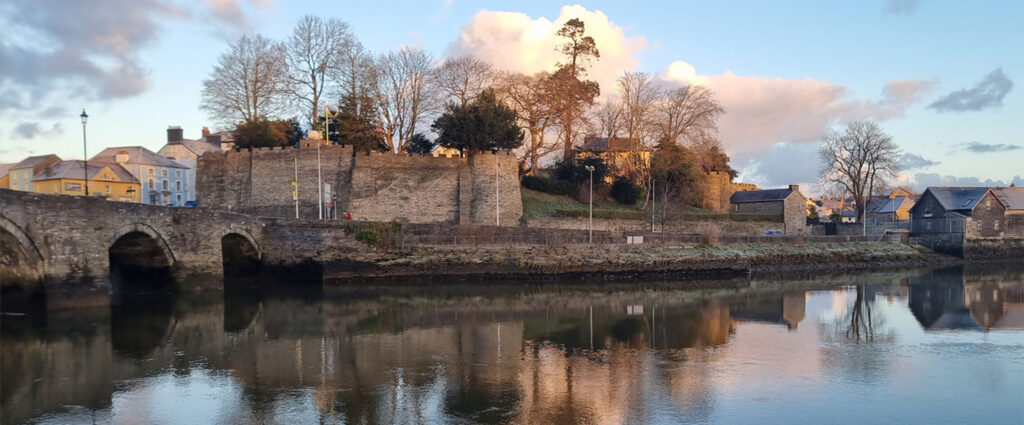 Sunset view of Cardigan Castle with reflective river and ancient bridge in Wales