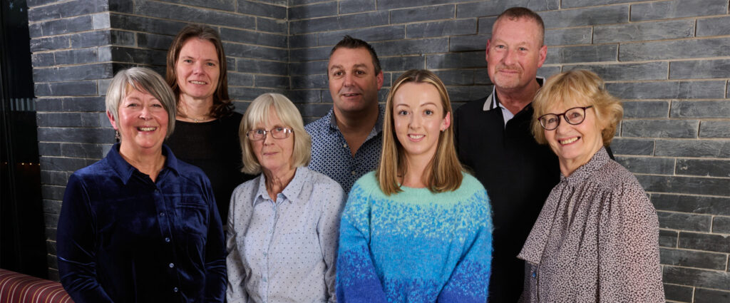 Multigenerational family smiling together against a stone wall, symbolizing community near Cardigan Castle.
